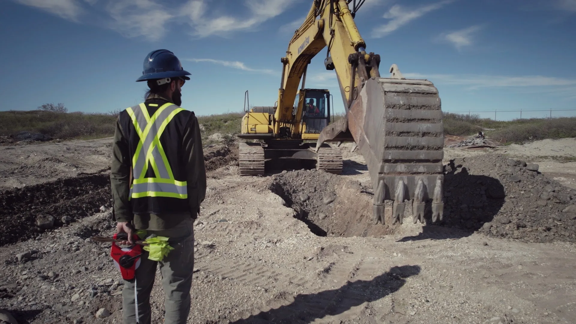 Worker supervising excavator at a remediation site under blue sky
